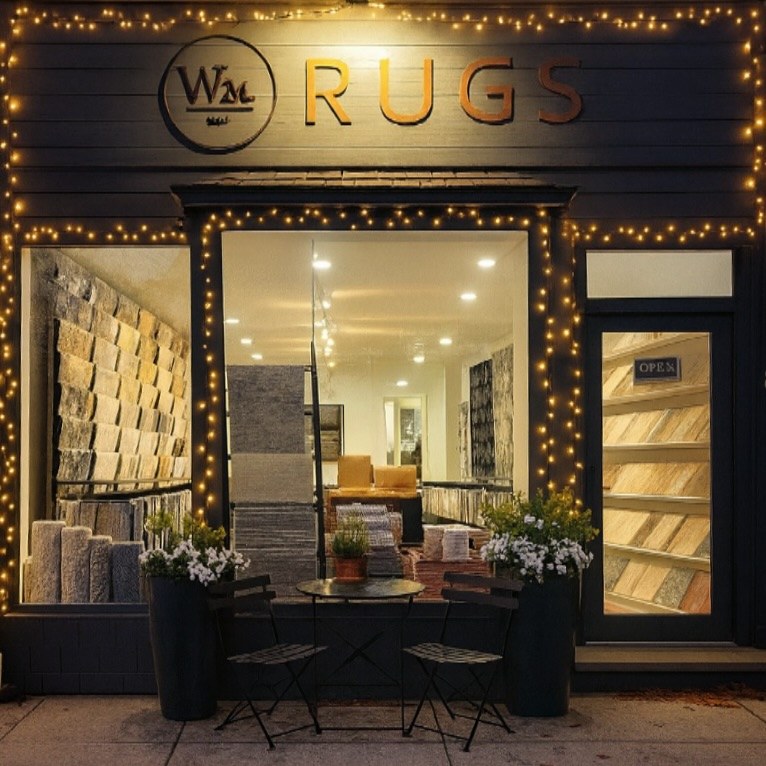 W.M. Sisal Rugs showroom storefront in Southampton at dusk, warm lights and rug samples in the window